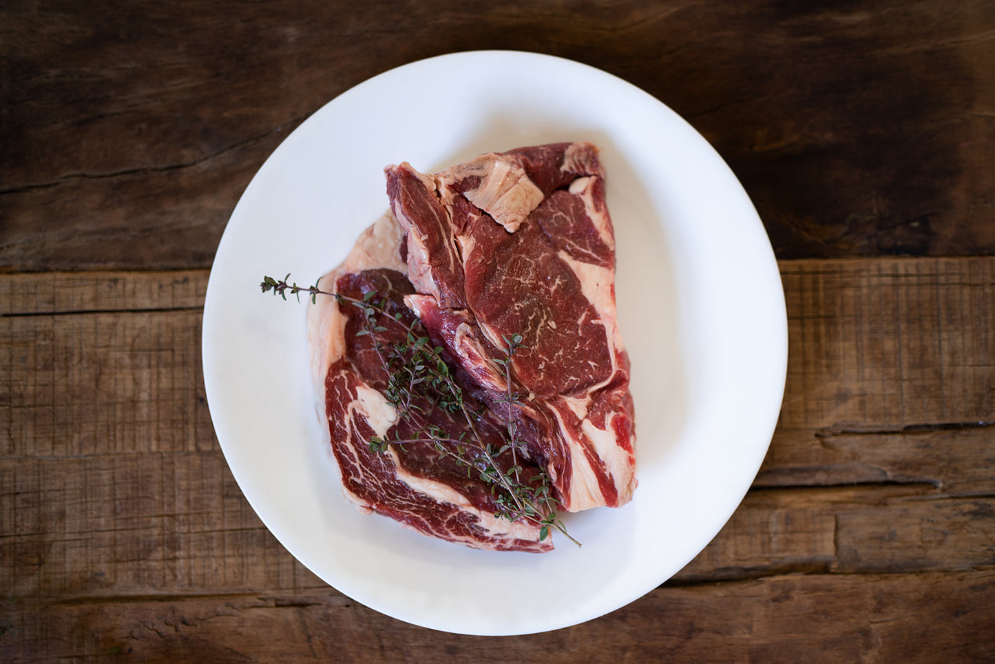 Two raw New York steaks with herbs on a white plate with a wooden background