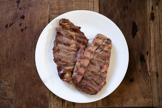 Two grilled New York Steaks on a white plate with a wooden background